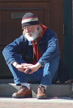 an old man sitting on the steps with his feet crossed and wearing a beanie