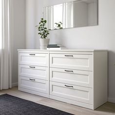 a white dresser with drawers and a mirror on the wall next to a potted plant