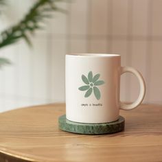 a white coffee mug sitting on top of a wooden table next to a potted plant