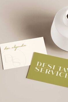 two business cards sitting on top of a table next to a white vase and paper