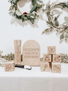 wooden blocks that say decorate a block for baby on a white table with greenery