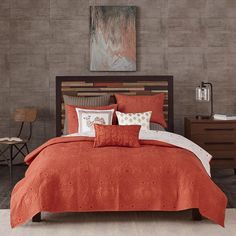 a bed with an orange comforter and pillows on top of it in a room