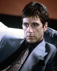 a man in a suit and tie sitting on a couch looking at the camera with an intense look