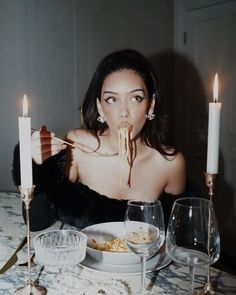 a woman sitting at a table eating spaghetti with two candles in front of her face