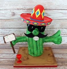 a green cactus with a red hat and sunglasses holding a sign