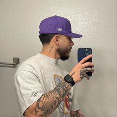 a man taking a selfie with his cell phone while wearing a purple baseball cap