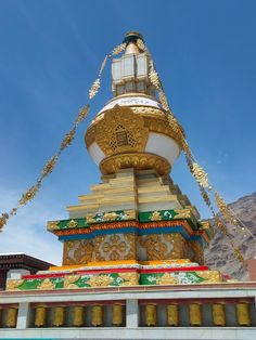 a large golden and white tower with a clock on it's side in front of mountains