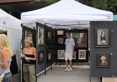 a man and woman are standing in front of some art on display at an outdoor market