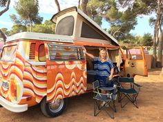 a woman standing in front of an orange and white camper van with the door open