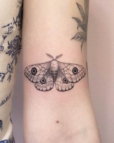 a small moth tattoo on the left inner arm and wrist, with two eyes in it