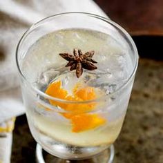 an orange peel and star anise sit in a wine glass filled with ice water