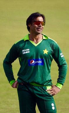 a man standing on top of a field wearing a green shirt and pants with his hands on his hips