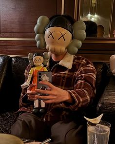 a person sitting on a couch holding a cell phone and wearing a balloon head mask