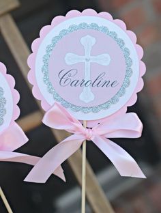 two pink and silver cupcake toppers with a cross on them, sitting on a stick