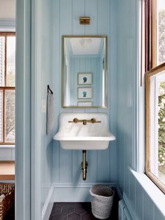 a bathroom sink sitting under a mirror next to a window in a blue painted room