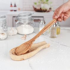 a person holding a wooden spoon on top of a counter next to jars and spices