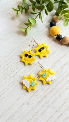 three yellow sun shaped earrings sitting on top of a wooden table next to green leaves