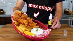 a person holding a basket filled with fish and fries next to a bottle of mayonnaise