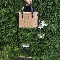 a person is holding a wicker bag in front of a bush with white flowers