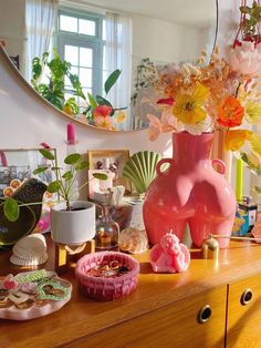 a dresser topped with pink vases filled with flowers and seashells next to a mirror