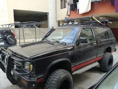 a black truck parked in front of a building next to a car with a rack on it's roof