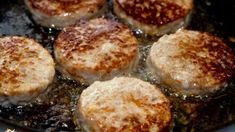 four hamburger patties cooking in a skillet with oil on the bottom and brown sugar on top