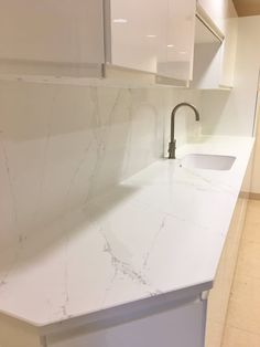 a white kitchen with marble counter tops and cabinets in the back drop off area is shown