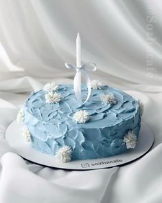 a blue frosted cake with white flowers and a single candle on top is sitting on a plate