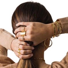 a woman with her hair in a ponytail wearing gold rings and bracelets, holding her hands on the top of her head