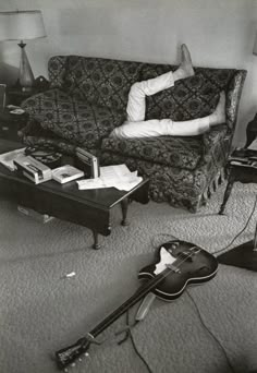 a man laying on top of a couch in a living room next to a guitar