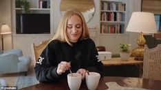 a woman sitting at a table holding two cups