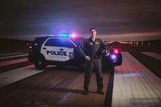 a man standing next to a police car on the road at night with its lights on