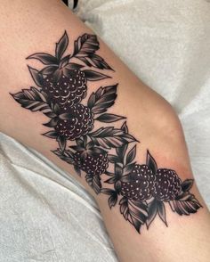 a black and white tattoo on the leg of a woman with berries growing out of it