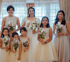 a group of women standing next to each other in front of a window holding bouquets