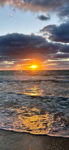 the sun is setting over the ocean with clouds in the sky and waves on the beach