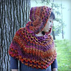 a woman standing next to a tree wearing a multicolored knitted shawl