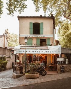 an old french restaurant with green shutters on the windows and people sitting at tables outside