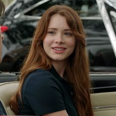 a woman with long red hair sitting in a car talking to another woman who is wearing a black shirt