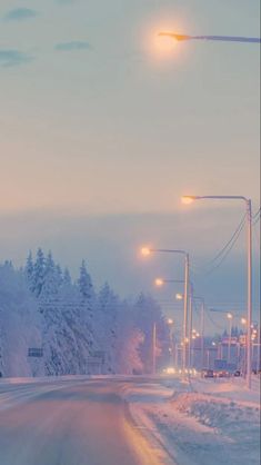 an empty street is covered in snow and lights are shining on the trees behind it