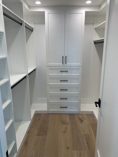 an empty walk - in closet with white cabinets and drawers on the wall, next to a wooden floor