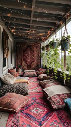 an outdoor covered porch with lots of pillows and rugs on the floor, lights strung from the ceiling