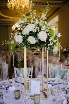 an elegant centerpiece with white flowers and greenery is displayed on a gold frame