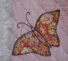 an embroidered butterfly is sitting on a piece of pink fabric with yellow and white flowers