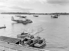 black and white photograph of boats in water with planes flying over them on top of the water