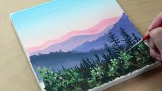 a person is painting a landscape with watercolors on a piece of paper that they are holding in their hands