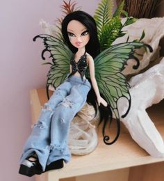 a doll sitting on top of a wooden table next to a plant and some feathers