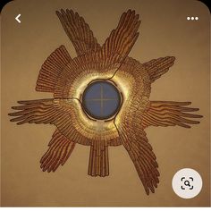 an image of a gold wall decoration with wings on it's side and a round window in the middle