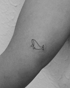 a black and white photo of a person's arm with a small whale tattoo on it