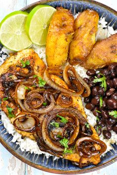 a blue plate topped with rice, beans and chicken next to two lime wedges