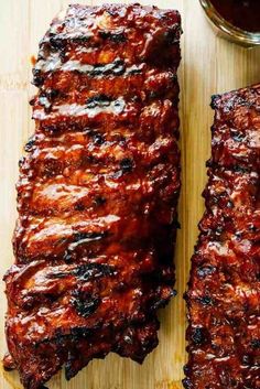 two pieces of barbecue ribs sitting on top of a cutting board next to a bowl of bbq sauce